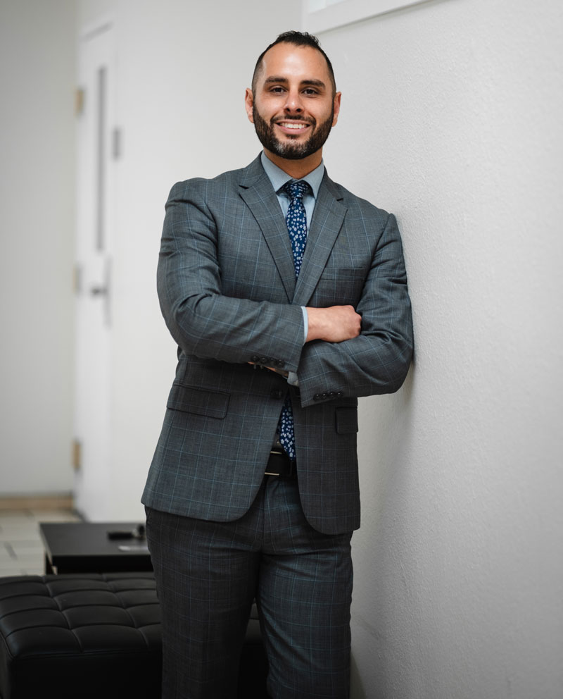 Contact Garcia Legal, Jonathan A. Garcia, accident and injury attorney, wearing a suit and smiling while leaning against a white wall